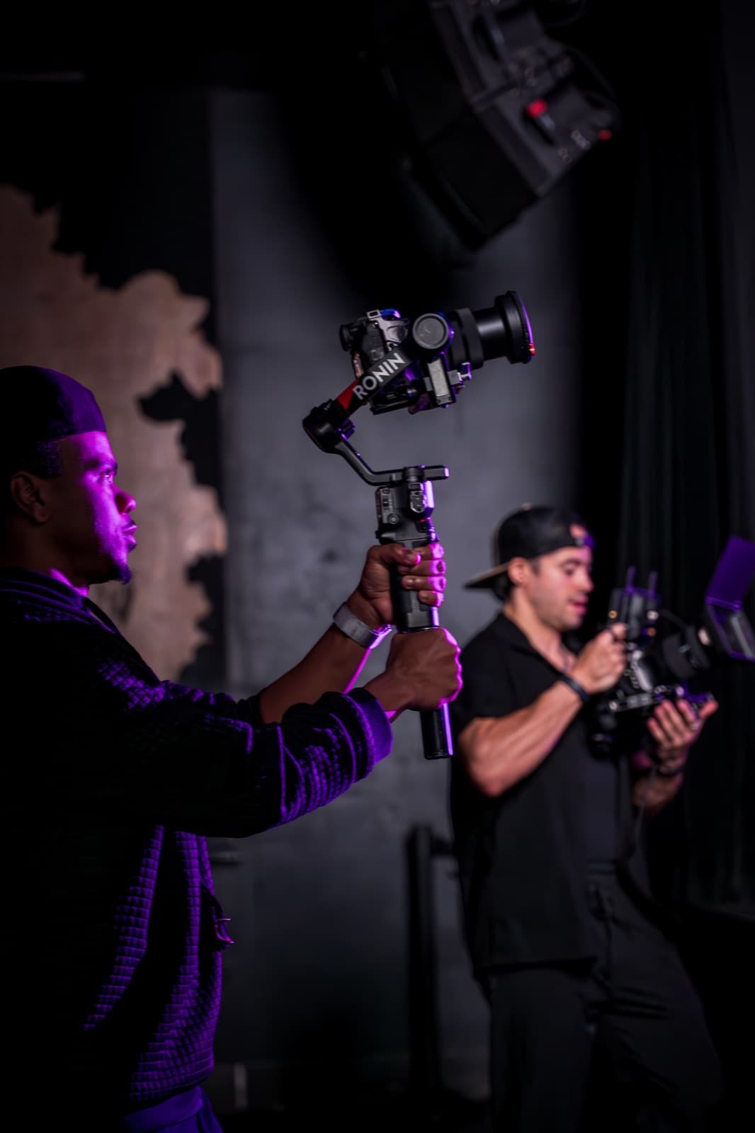 A MediaGeekz camera operator filming with a gimbal on a purple-lit stage
